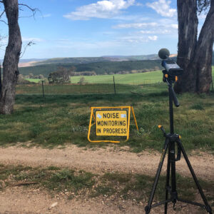 microphone in field with a sign saying 'noise monitoring in progress'