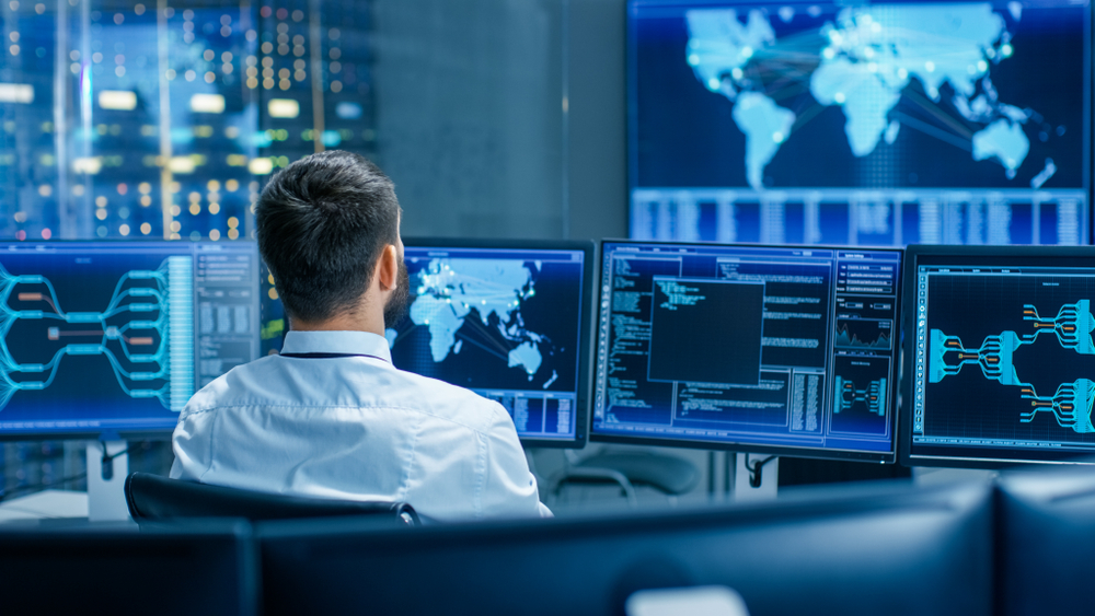 Man sitting in control room looking at multiple screens