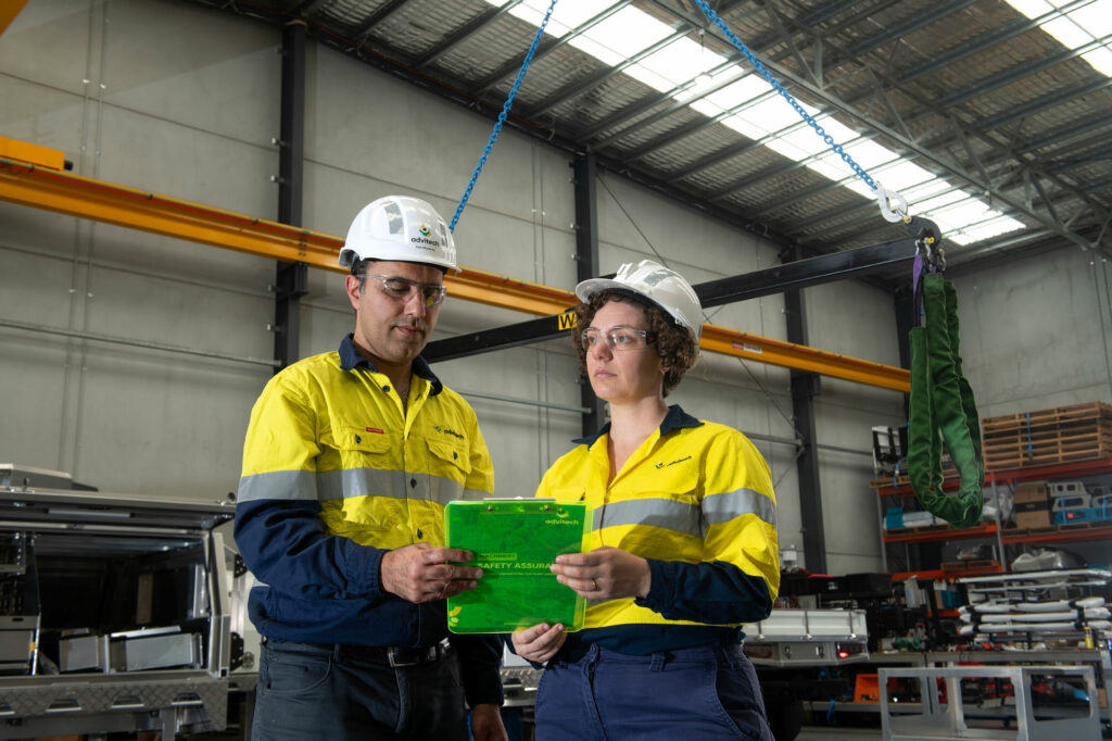 A man and woman in PPE clothing inspecting electrical controls in a factory